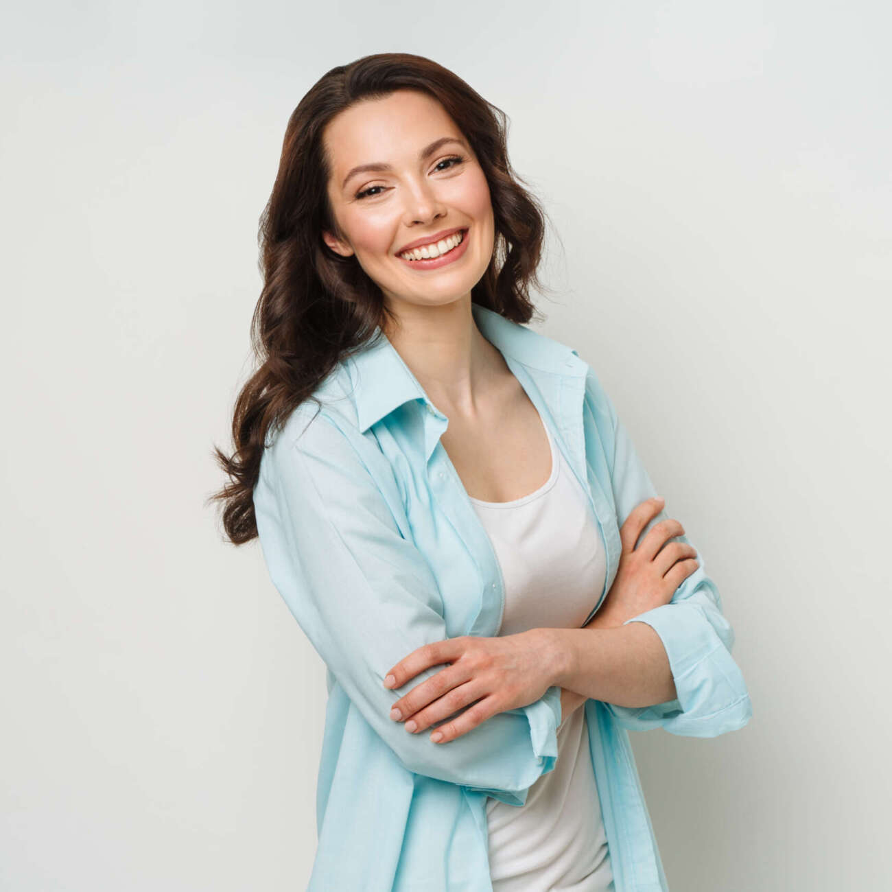 Young woman portrait. Adorable brunette in a shirt looking at the camera with her arms crossed,